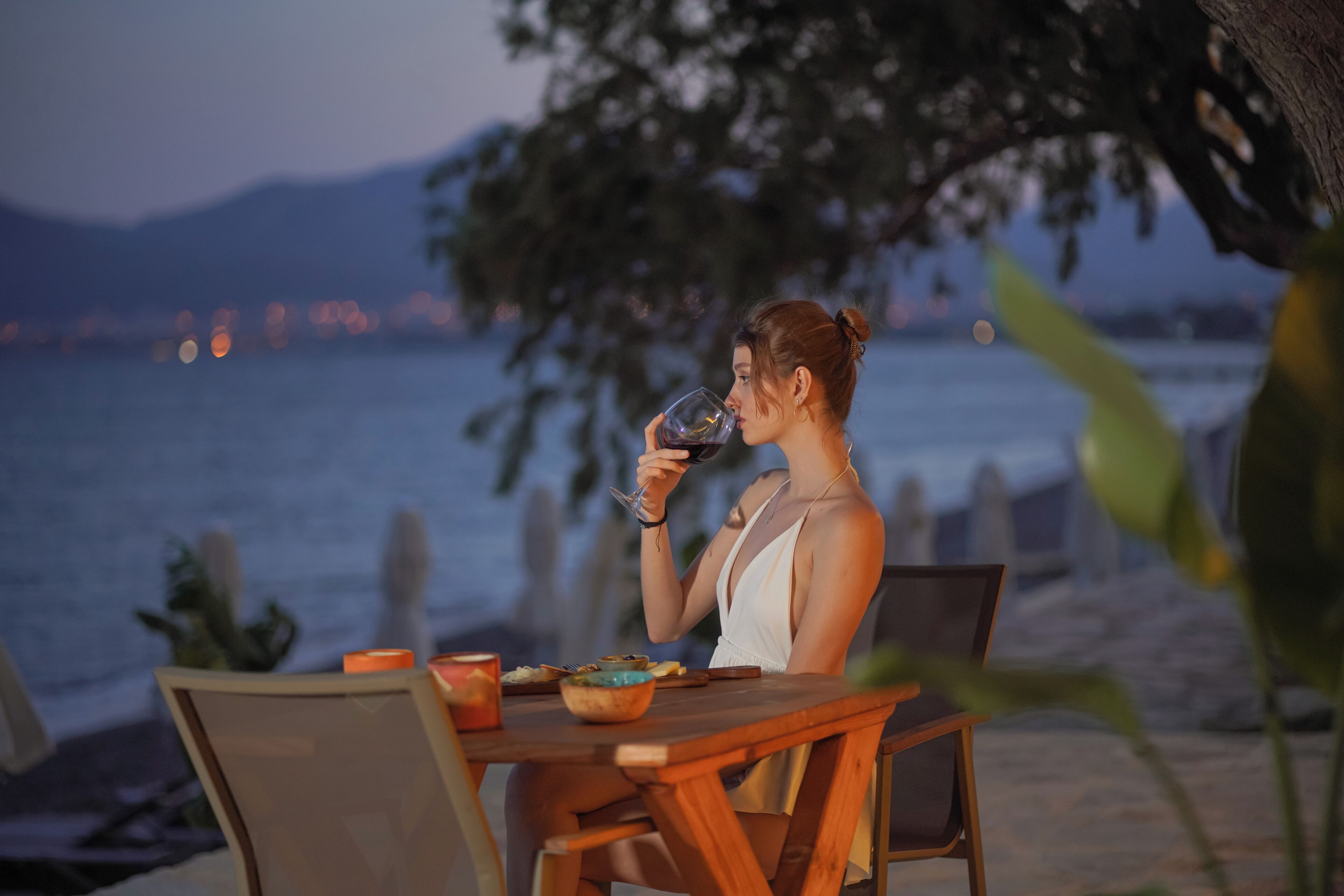 A person sitting at a wooden table by the seaside, holding a glass.