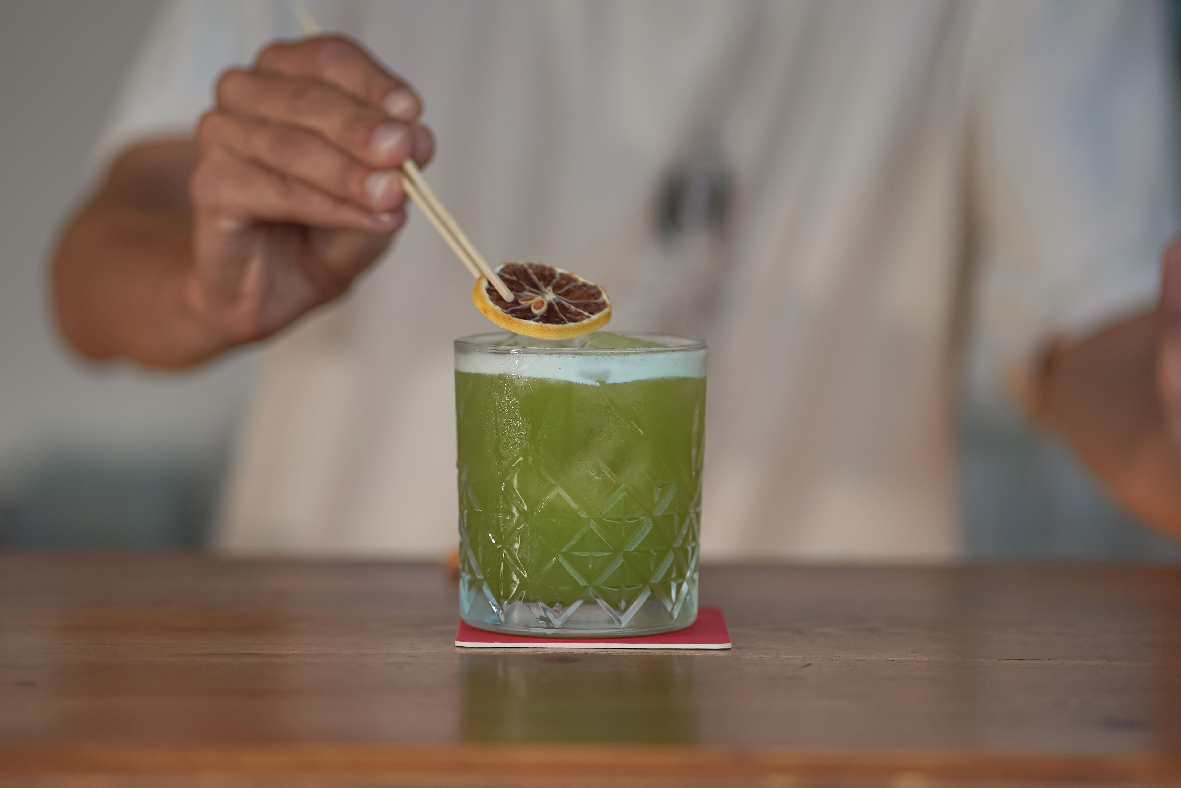 A person holding a cocktail with a lemon slice garnish.