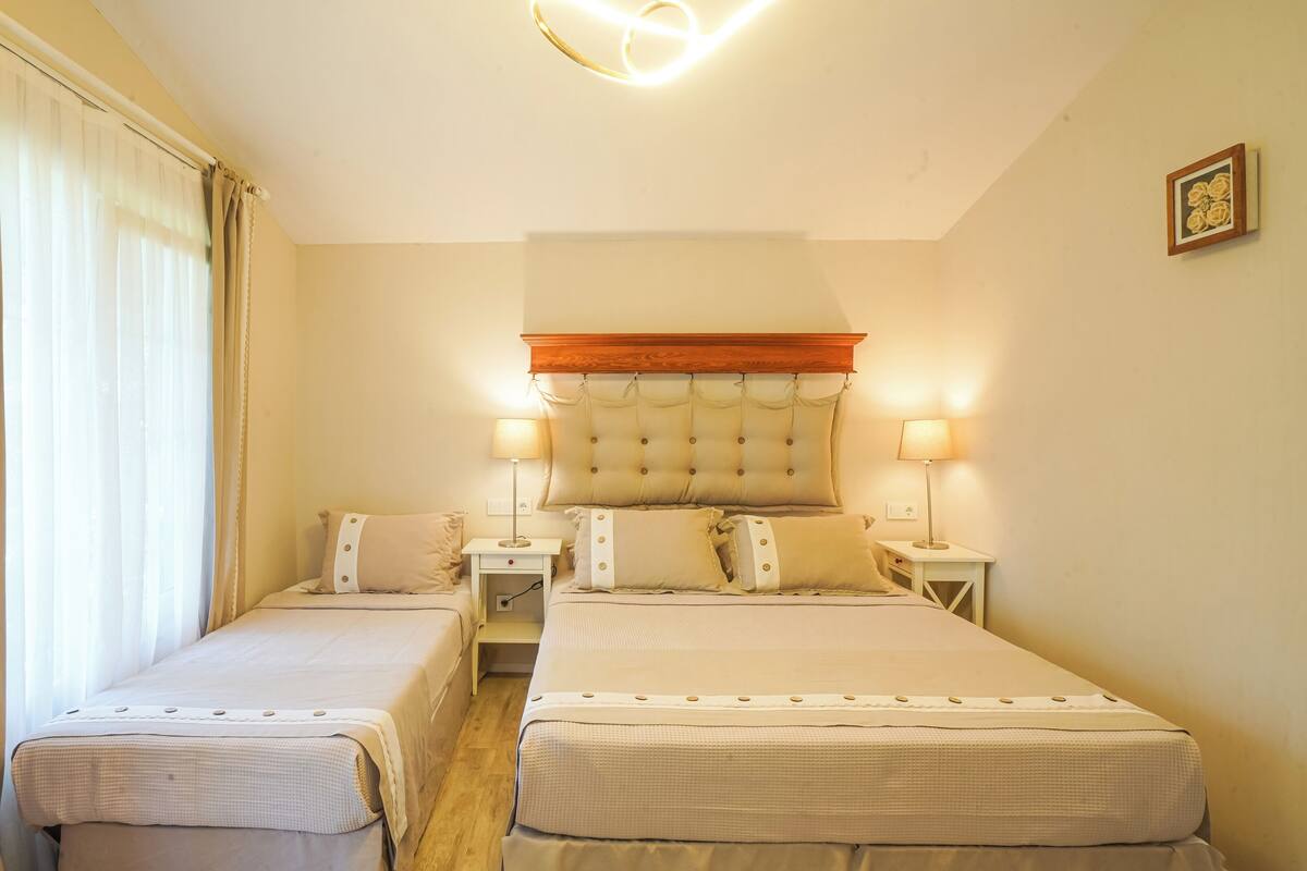 A hotel room with two beds, a wooden headboard, bedside lamps, and a small table.