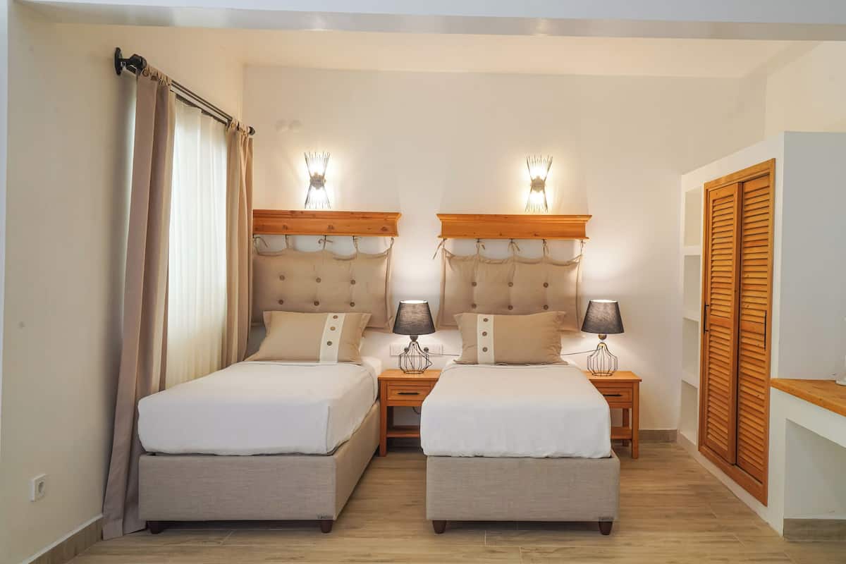 A double room with two beds, bedside tables with lamps, a wooden wardrobe, and a small table with candles.