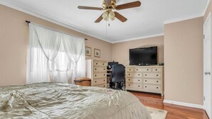 Une chambre à coucher avec un lit, un bureau, une télévision et un ventilateur de plafond.