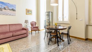 Una sala de estar con un sofá, una mesa de comedor redonda con sillas, un aparador de vidrio y una lámpara.