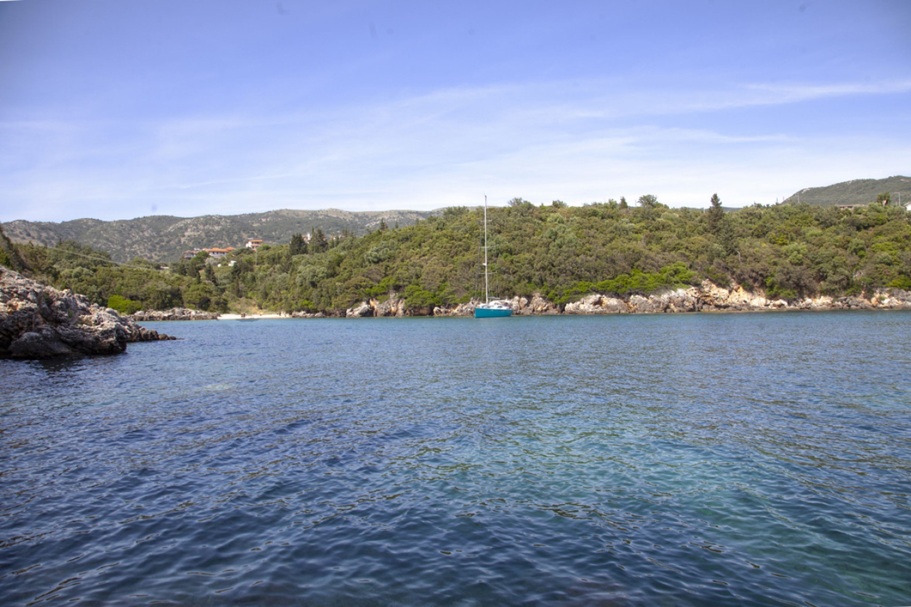 Eine Küstenlandschaft mit klarem Wasser, einem Boot und einer hügeligen Landschaft mit vereinzelten Gebäuden.