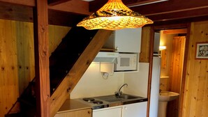 Een keuken met een houten trap, een eettafel met een fruitschaal, en een hangende lamp.