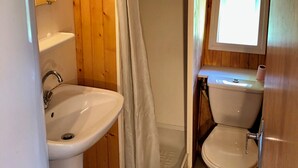 Een badkamer met houten inrichting, een douche met gordijn, een wastafel en een toilet.