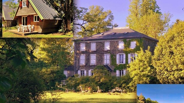 Een houten chalet met een veranda en zitplaatsen buiten, een groot gebouw van steen met meerdere ramen en een tuin, en uitzicht op een meer omringd door bomen.