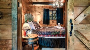 Ein Schlafzimmer einer Holzhütte mit einem Bett, einer Lampe und einem kleinen runden Tisch.