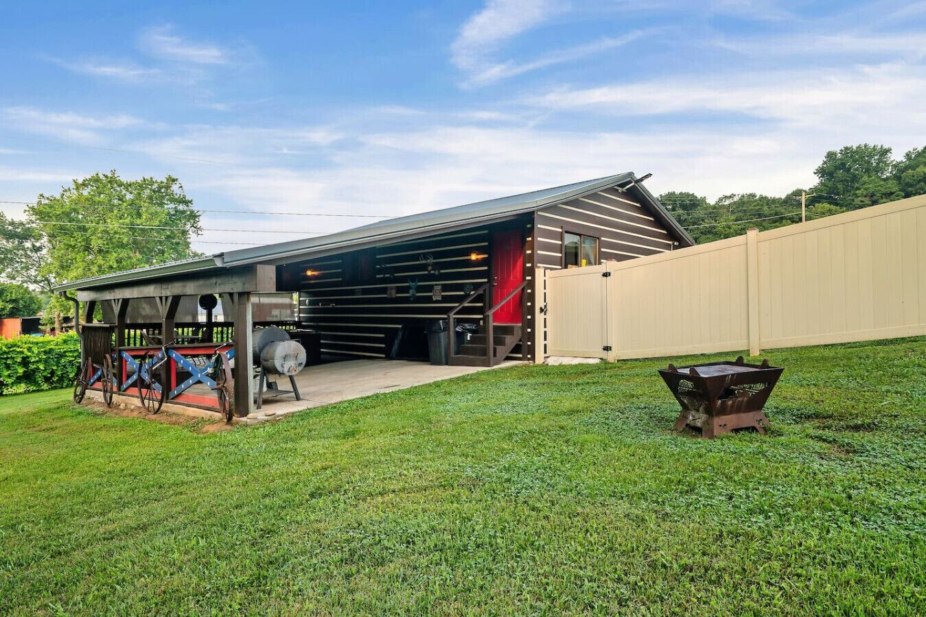 A covered outdoor area with a barbecue grill, a wooden fence, and a grassy lawn.