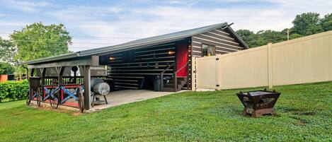 A covered outdoor area with a barbecue grill, a wooden fence, and a grassy lawn.