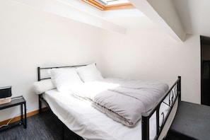 Cozy retreat with a single bed, bedside table, and lamp, set against a sloping ceiling with a skylight.