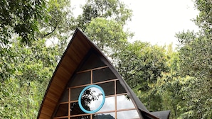 Een houten hut met een groot rond raam, een blauwe deur en een stenen bank ervoor.