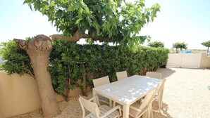 Un espace extérieur aménagé avec une table et des chaises, entouré d’une haie et d’un arbre.