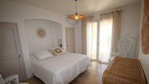Une chambre à coucher avec un lit, un luminaire suspendu, une chaise et une table d’appoint en osier.