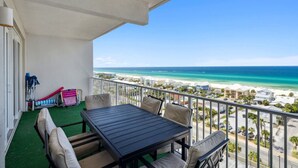 A balcony with a table and chairs, a view of the beach, and a clear sky. - Ocean Views-5 Pools-Hot Tub-Shops LTW 1006 (Panama City Beach)
