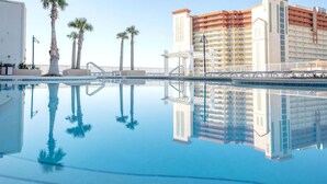 A clear pool with reflections of palm trees and a hotel building. - Ocean Views-5 Pools-Hot Tub-Shops LTW 1006 (Panama City Beach)
