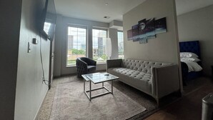 Een moderne woonkamer met een bank, een glazen salontafel, een stoel en een aan de muur bevestigde televisie.