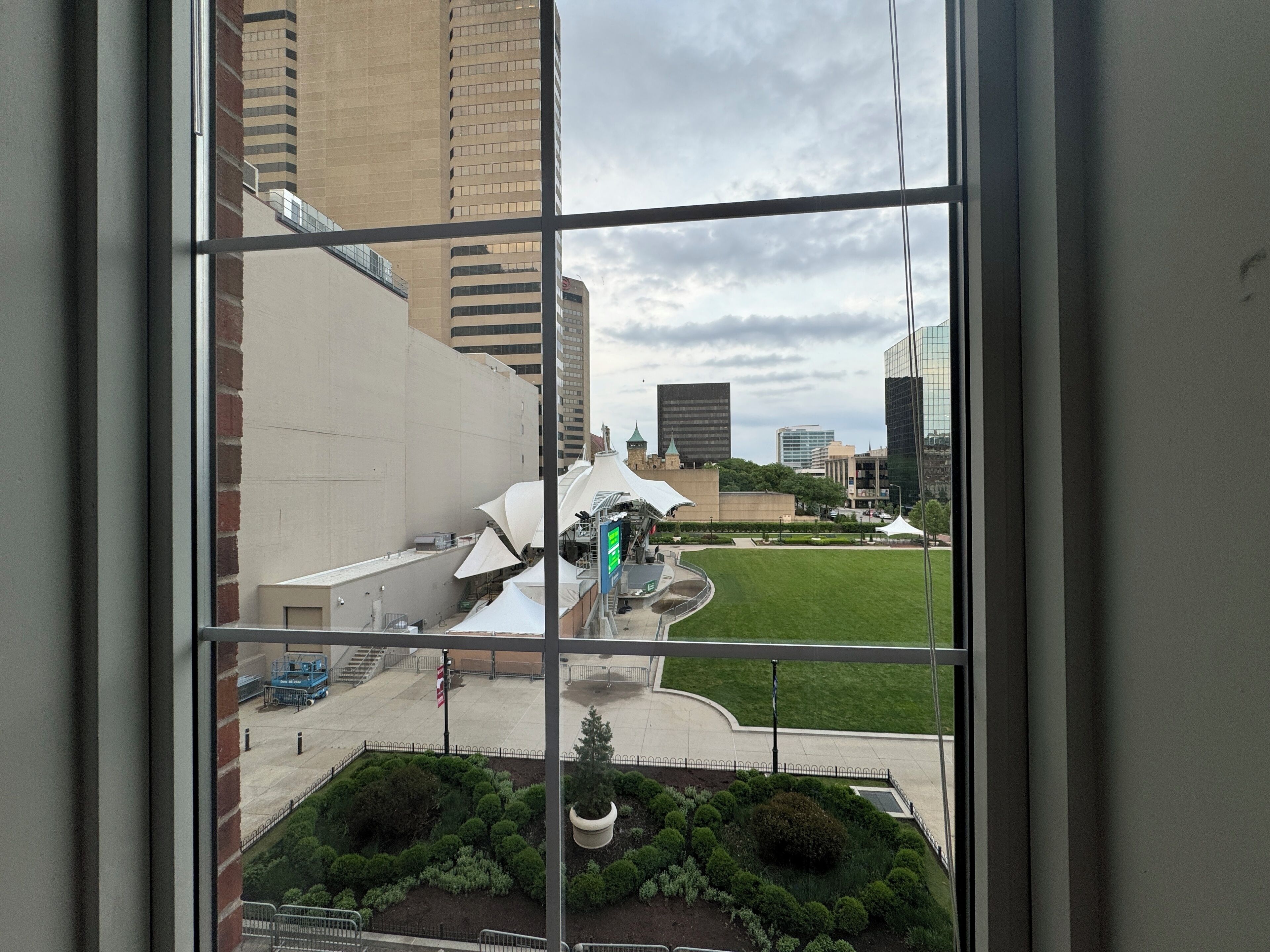 A view through a window of a building with a courtyard, a fountain, and surrounding greenery.
