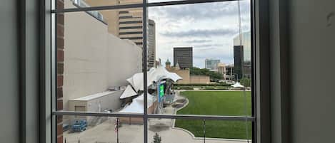 A view through a window of a building with a courtyard, a fountain, and surrounding greenery.