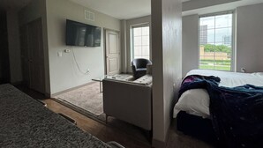 Een slaapkamer met een bed, een bureau, een stoel, een televisie en een raam met uitzicht op de stad.