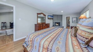 A bedroom with a bed, dresser, mirror, television, fireplace, and a door leading to another room.