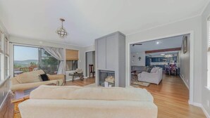 A spacious living room with a fireplace, a sofa, and a dining area visible through an open doorway.