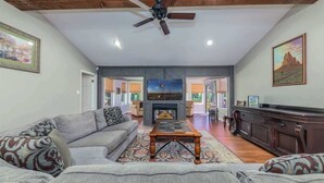 A spacious living room with a fireplace, a ceiling fan, and a large television.