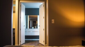 Ein Hotelzimmer mit einem Bett, einem Nachttisch und einer Tür zu einem Badezimmer mit Spiegel und Waschbecken.