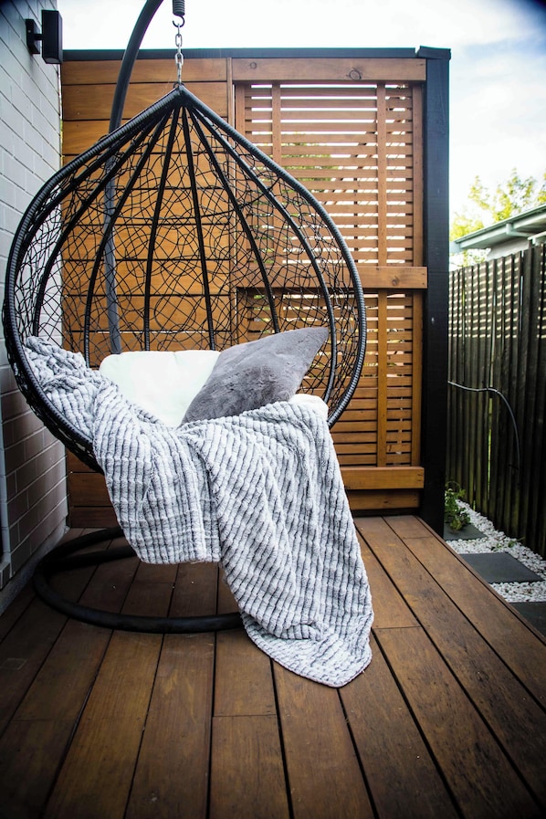 Relax in a cozy outdoor setting with a hanging chair suspended from a metal frame, perfect for a peaceful retreat.