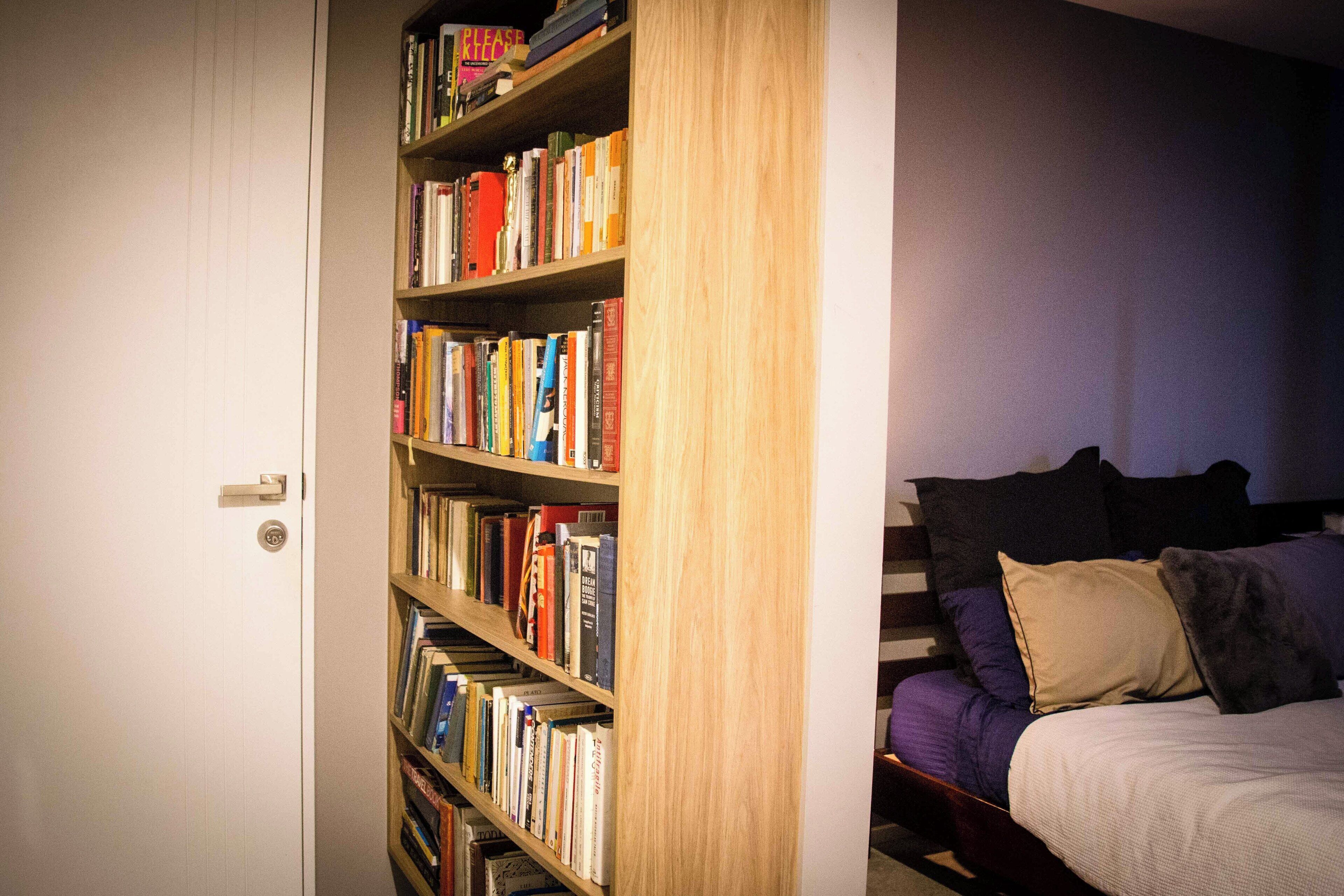 Un dormitorio con una estantería llena de libros, una cama con almohadas y una puerta con picaporte.