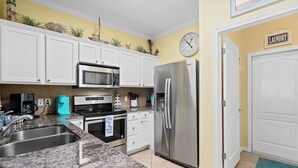 Eine Küche mit weißen Schränken, Edelstahlgeräten, einer Arbeitsplatte aus Granit und einer Uhr an der Wand.