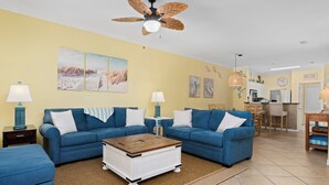 Ein Wohnzimmer mit zwei blauen Sofas, einem Holztisch und einem Deckenventilator.