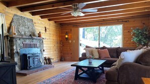 Ein gemütliches Blockhaus-Interieur mit Kamin aus Stein, Holzbalkendecke, einer Couch und einem Couchtisch.