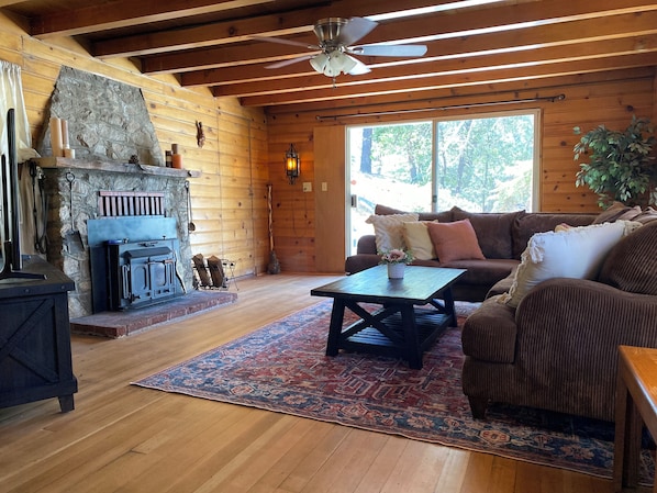 A cozy cabin interior with a stone fireplace, wooden ceiling beams, a sofa, and a coffee table.