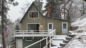 Eine zweistöckige Holzhütte mit einem Balkon, umgeben von Bäumen und einer verschneiten Landschaft.