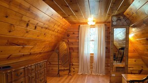 Ein Zimmer in einer Holzhütte mit einem Schminktisch, einem Spiegel, einem Stuhl und einem Fenster mit Vorhängen.