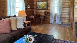 Ein gemütliches Holzhaus-Interieur mit einem braunen Sofa, einem kleinen Tisch, einem Stuhl und einem Bild an der Wand.