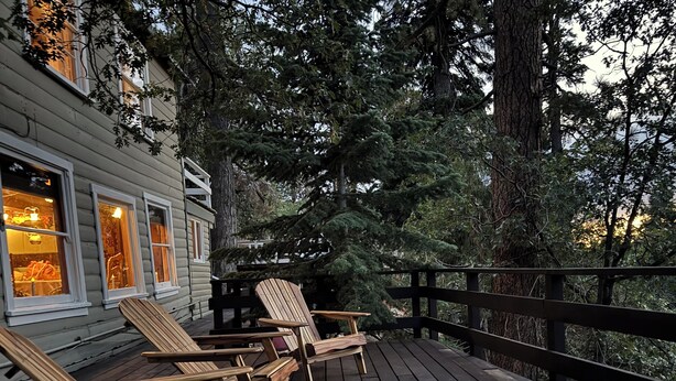 Eine Holzterrasse mit Adirondack-Stühlen, einer Geländer und einem Gebäude mit Fenstern.