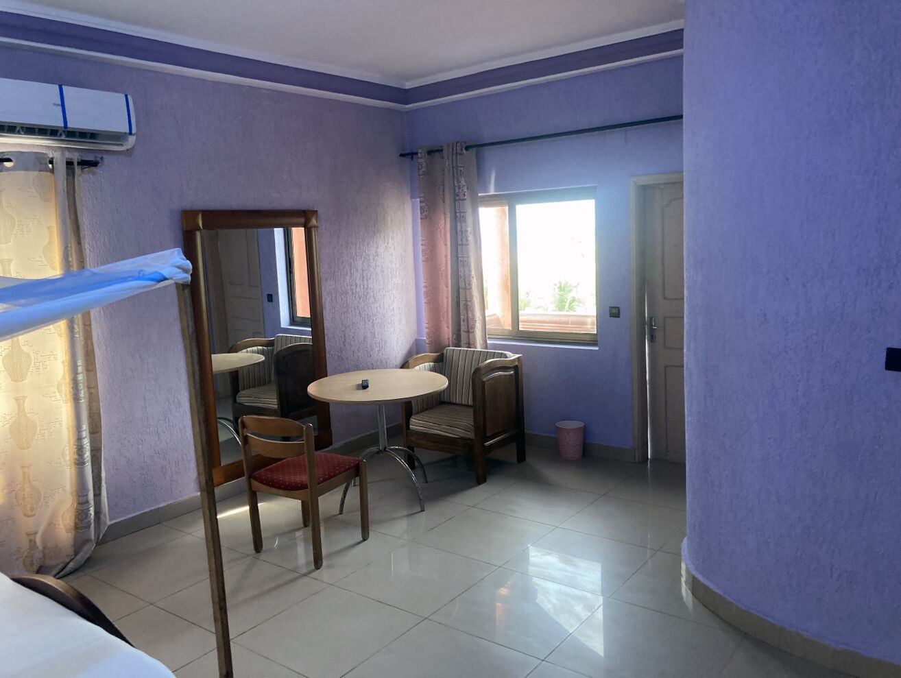 Una habitación con una mesa redonda, dos sillas, un espejo y una ventana con cortinas.