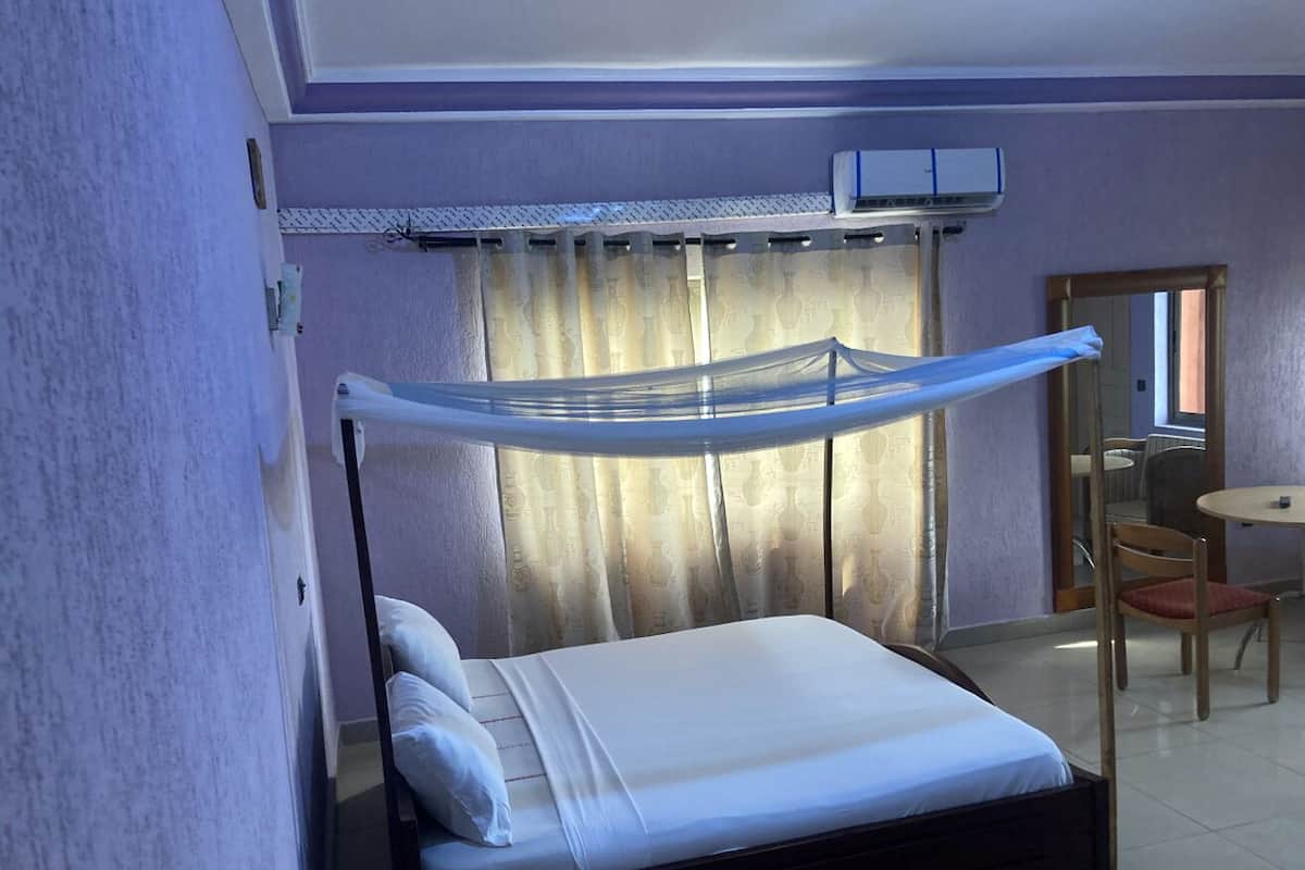 Un llit individual amb dosser, una taula rodona petita i una cadira en una habitació amb parets morades i un ventilador de sostre.