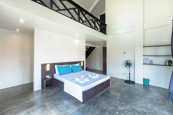 A modern hotel room with a large bed, a standing fan, and a staircase leading to an upper level.