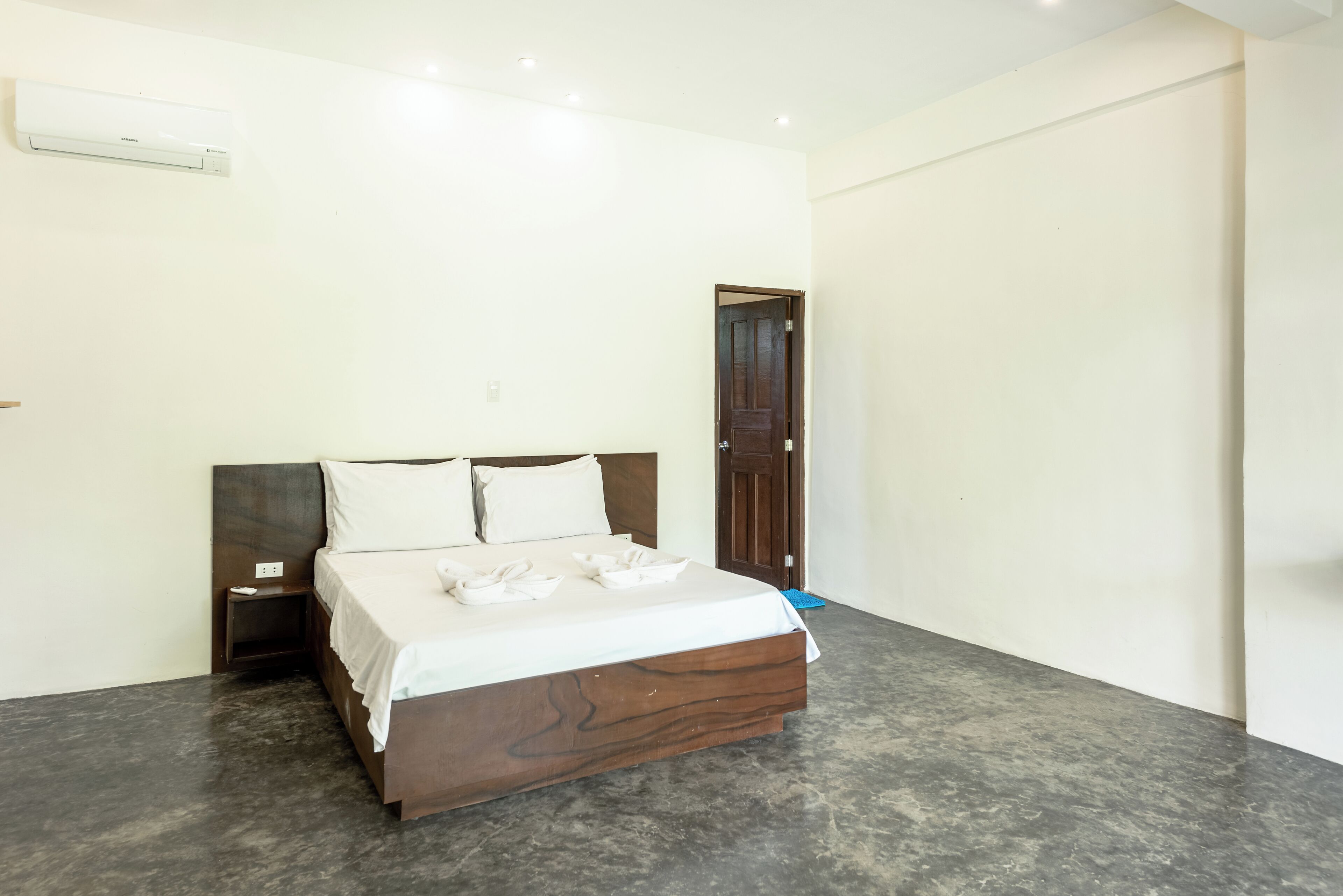 Een slaapkamer met een bed, nachtkastje, houten hoofdbord, een deur en een wandairconditioner.