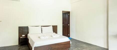 Een slaapkamer met een bed, nachtkastje, houten hoofdbord, een deur en een wandairconditioner.