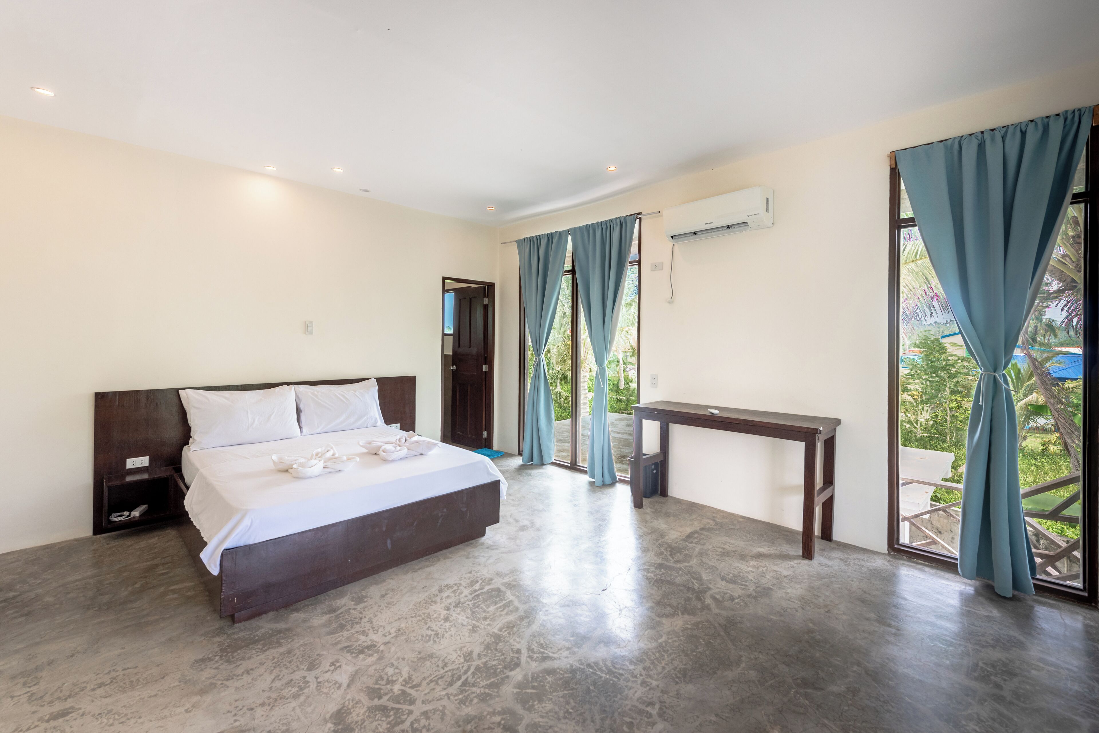 A bedroom with a bed, bedside table, and a view of the outdoors.