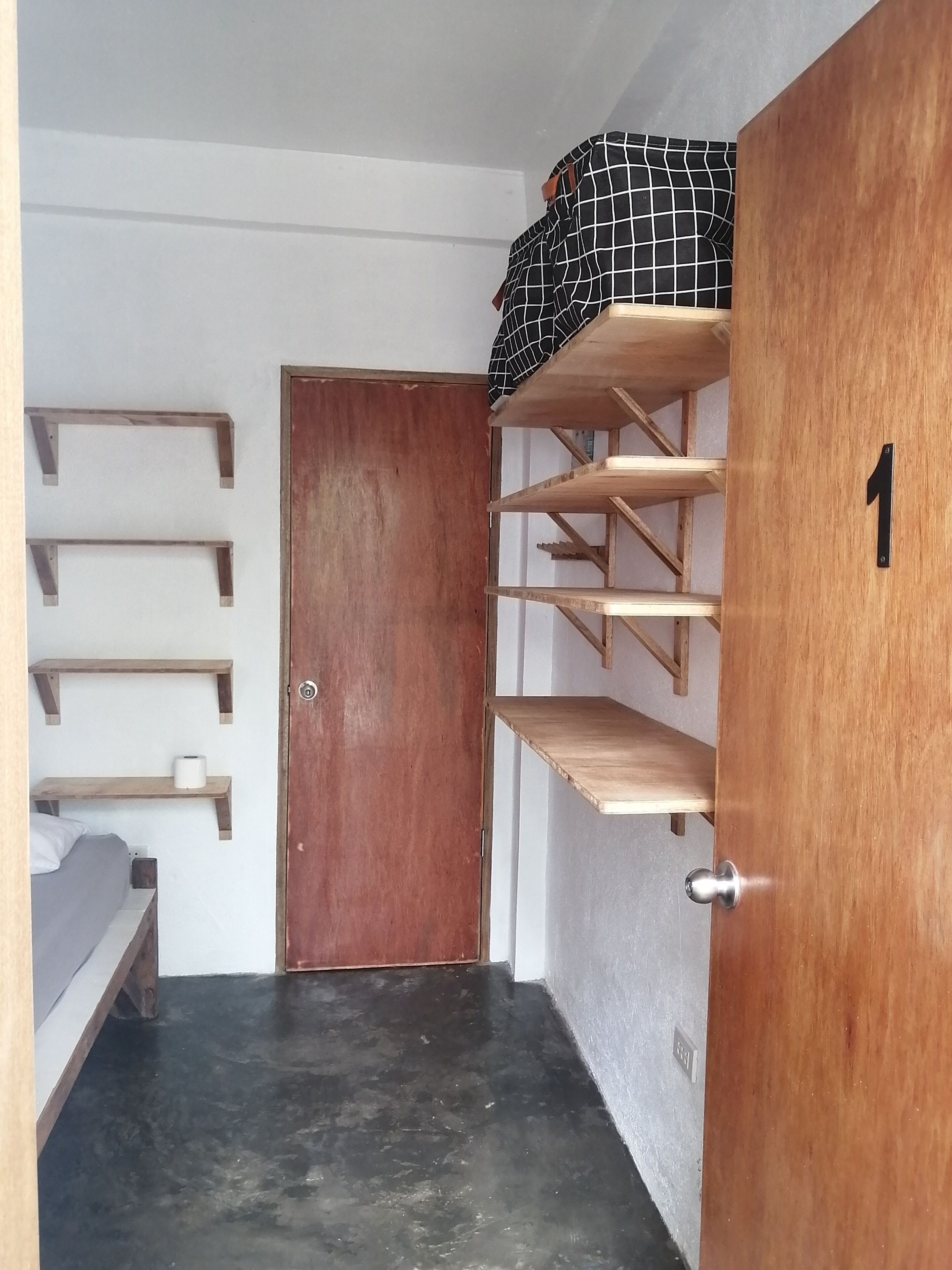 A room with a wooden door, a black and white checkered bag on a shelf, and multiple wooden shelves.