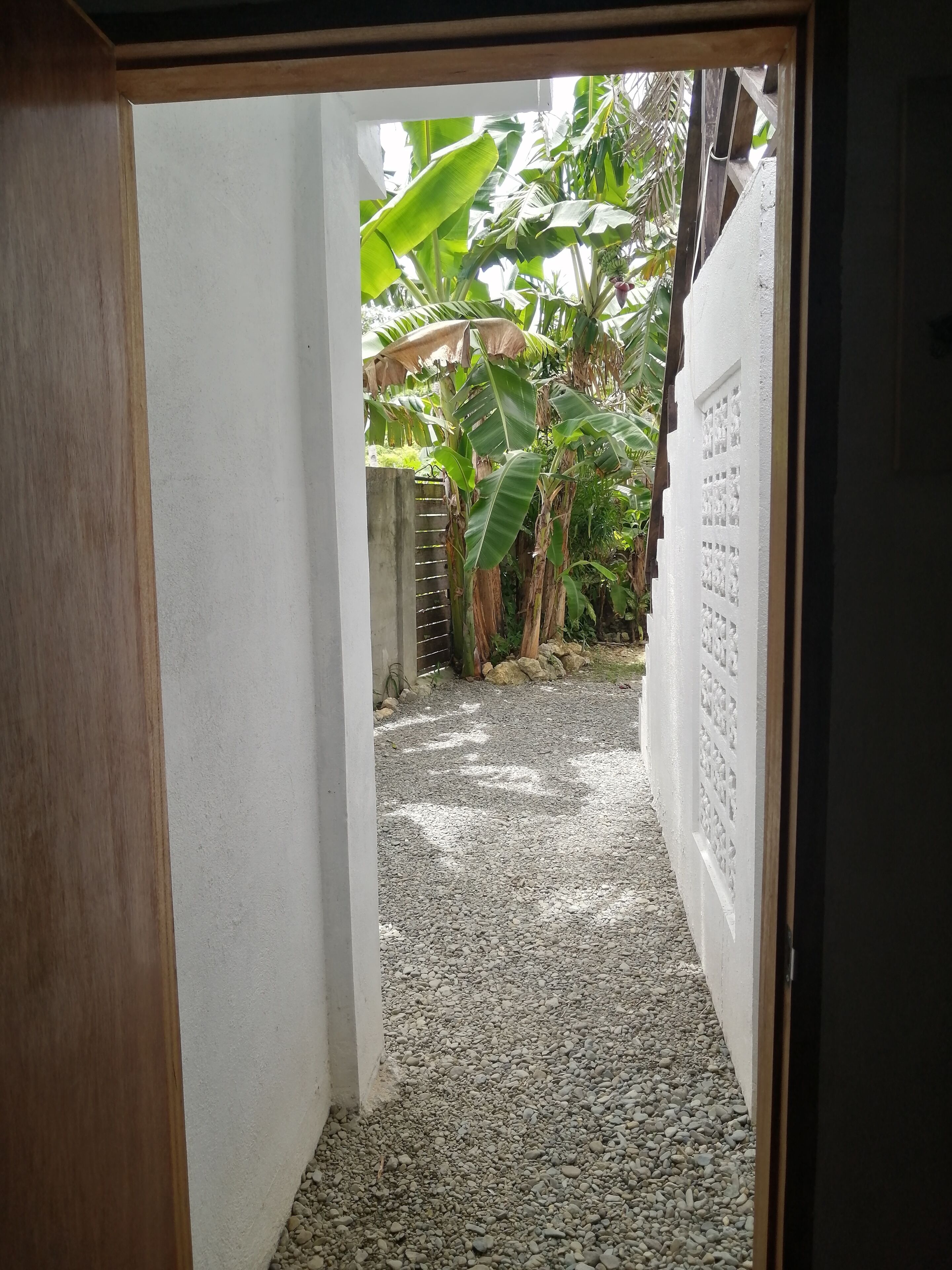 Un sendero estrecho que lleva a un jardín con suelo de grava y un muro blanco con un diseño decorativo.
