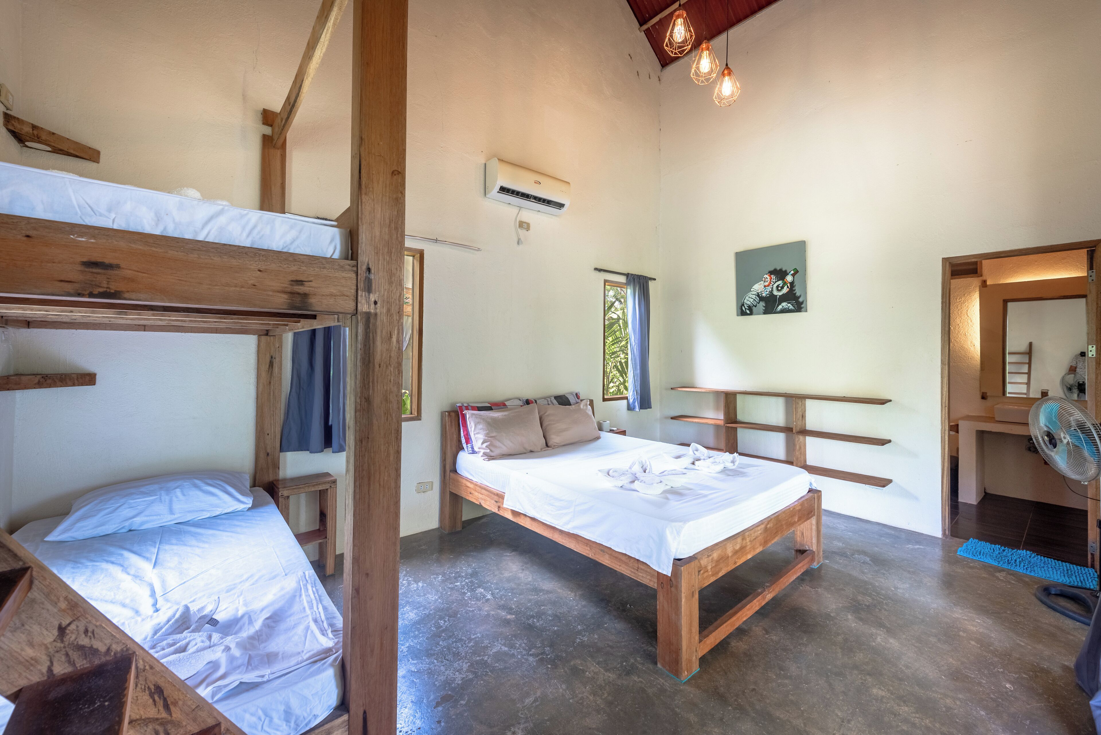A room with bunk beds, a wooden desk, an air conditioner, and a fan.