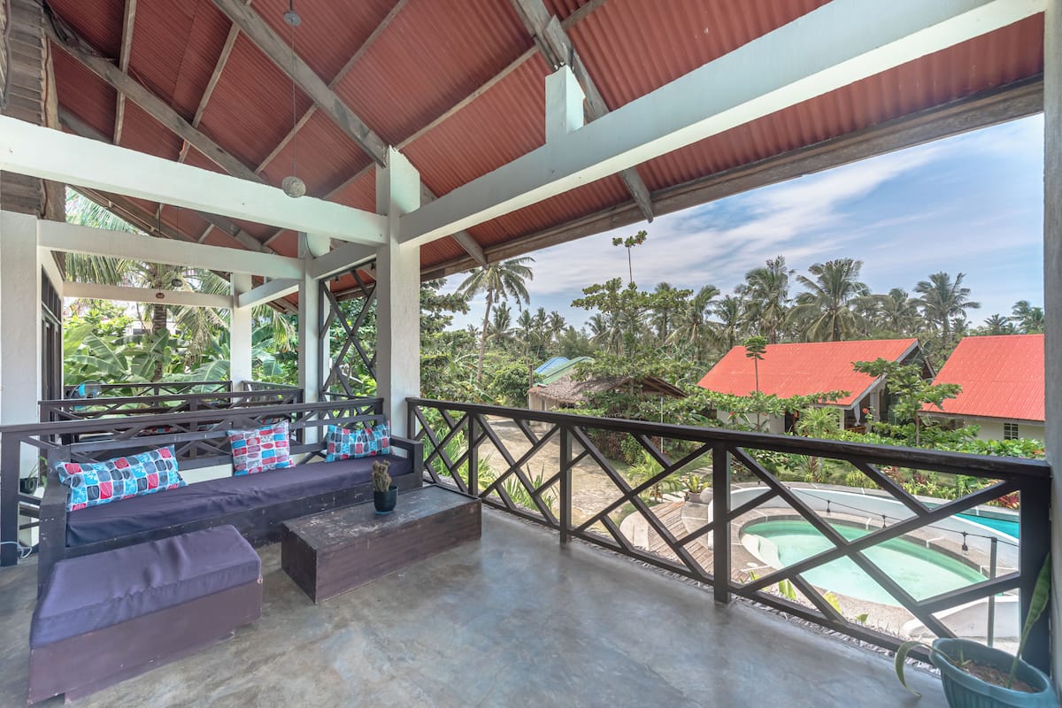 A covered outdoor seating area with a view of a pool and palm trees.