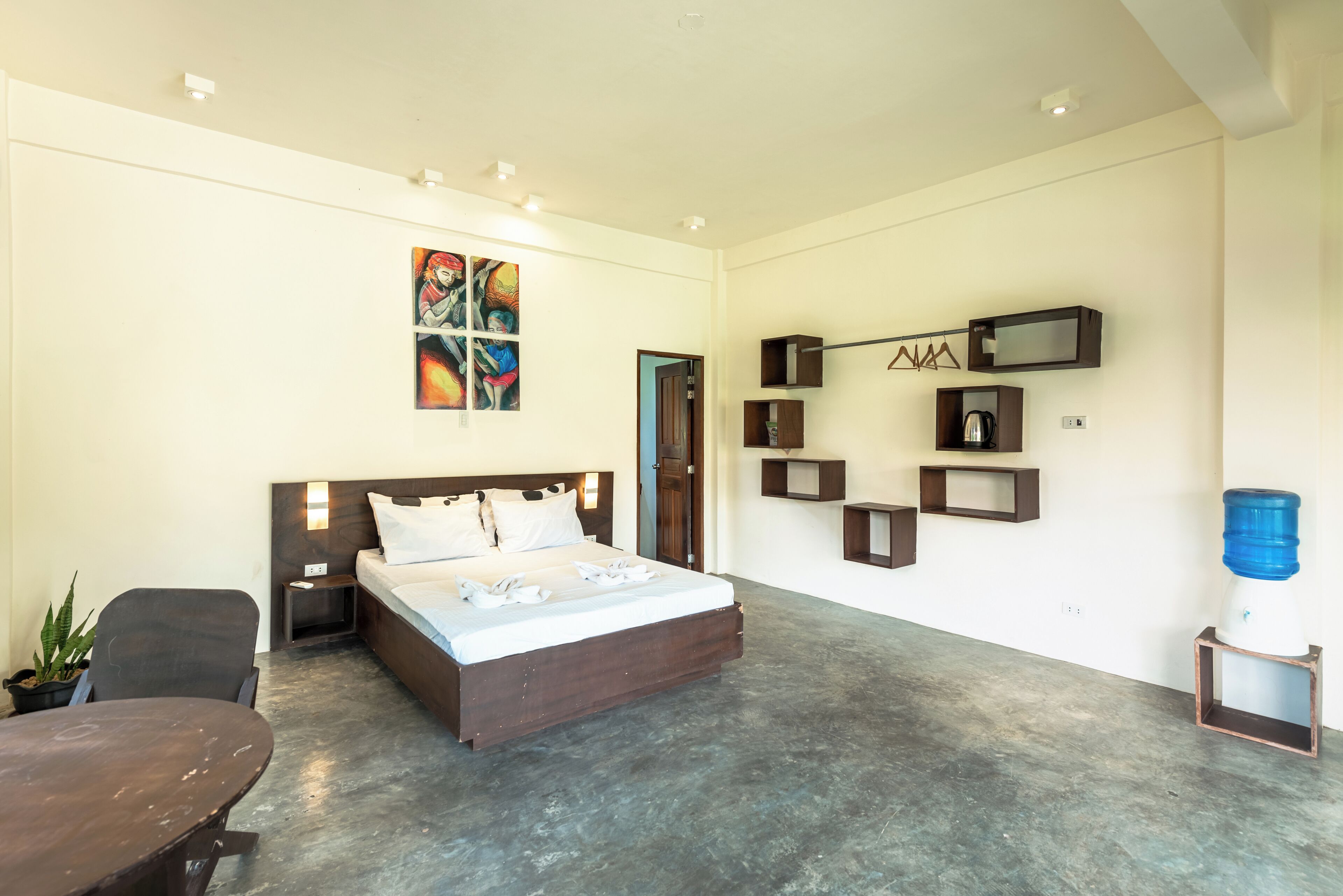 A modern bedroom with a large bed, bedside tables, a desk, and a water dispenser.