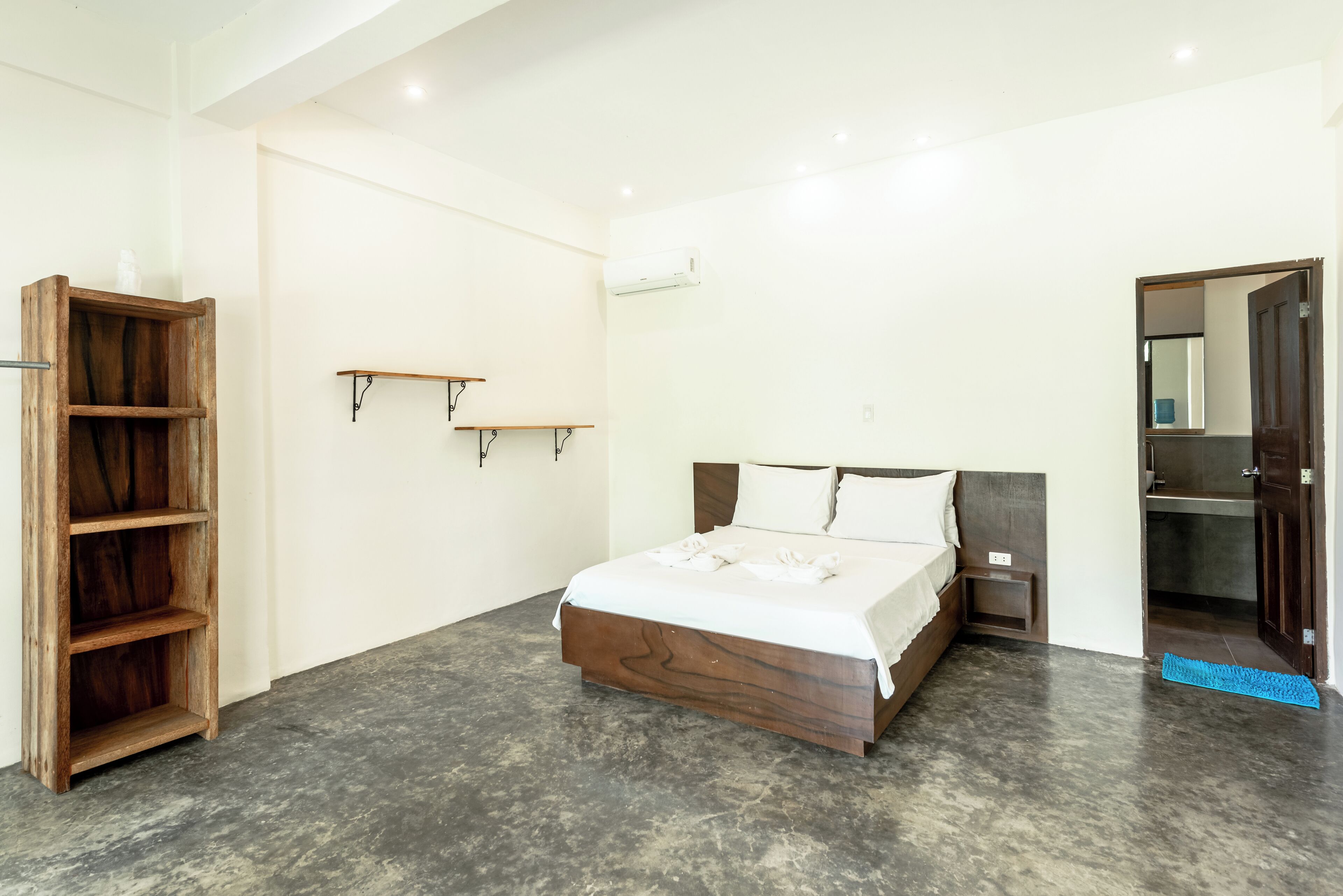 A bedroom with a wooden bed, a shelf, and a door leading to a bathroom.