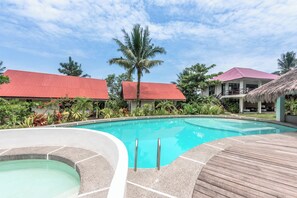 A swimming pool with a wooden deck and a hot tub, surrounded by lush greenery and buildings with red roofs. - Ohana Resort Siargao (General Luna)
